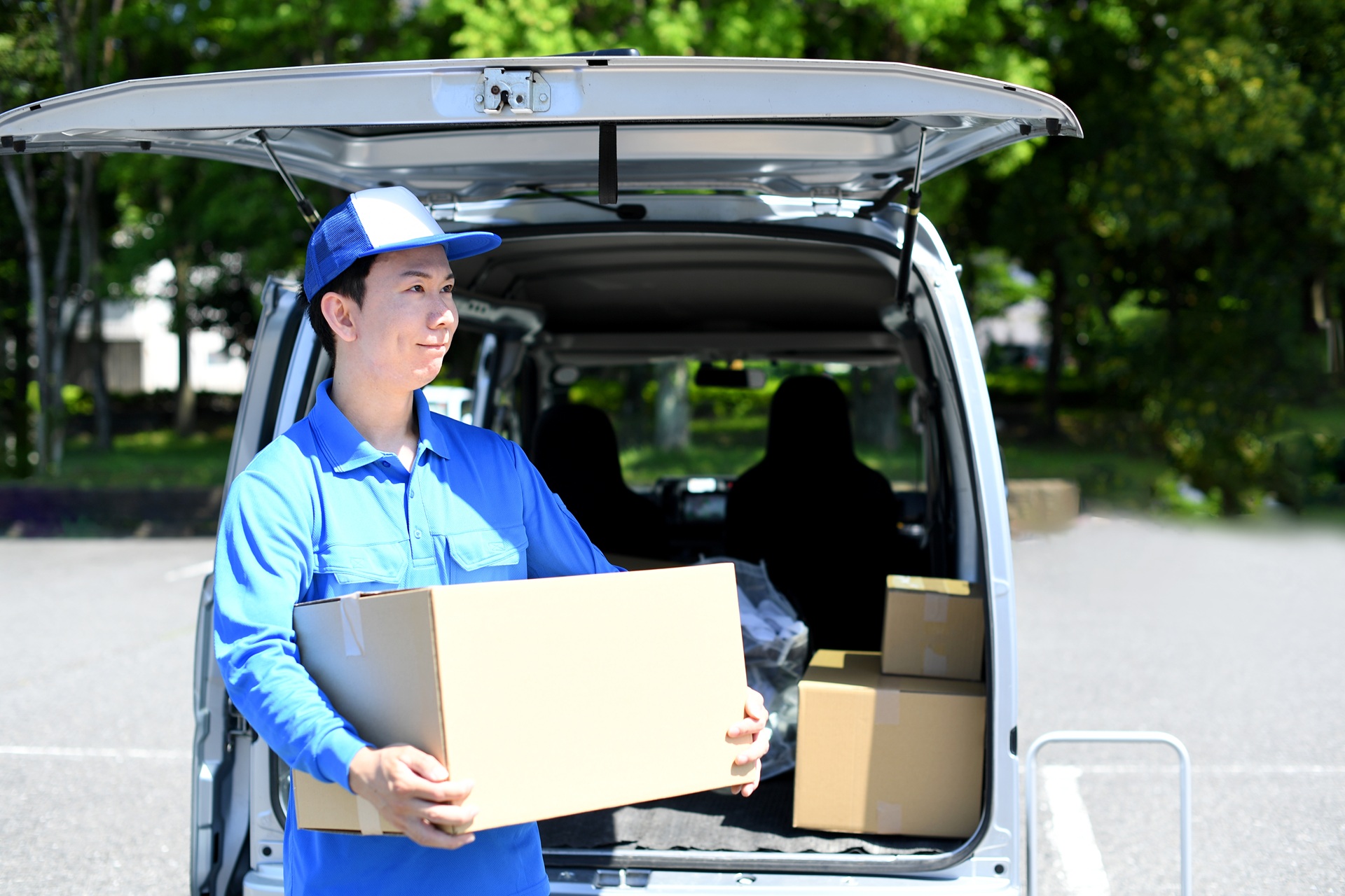 軽バンの前で荷物を運ぶアジア人男性配達員